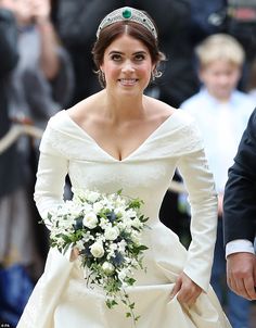 a woman in a wedding dress walking down the street with a bouquet on her hand