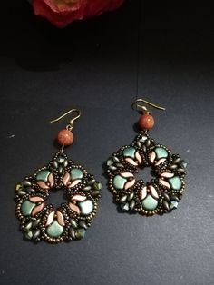 two pairs of earrings sitting next to each other on a black surface with a flower in the background