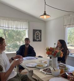 three people sitting at a table with food and drinks in front of them, talking to each other