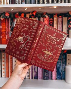 a hand holding two red books in front of a book shelf