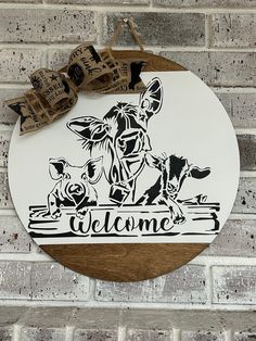 a welcome sign hanging on the side of a brick wall with a cow and two dogs