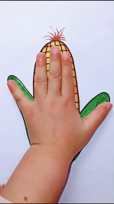 a child's hand holding an ornament with a corn on the cob design