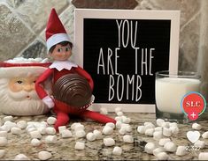 an elf is sitting next to marshmallows and a sign that says you are the bomb