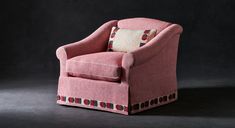 a pink chair sitting on top of a black floor next to a white and red pillow