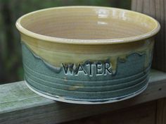 a yellow and green bowl sitting on top of a wooden table next to a fence