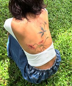 a woman sitting in the grass with her back turned to the camera and tattoos on her body