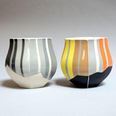 two vases sitting next to each other on a white tableclothed surface with lines painted on them