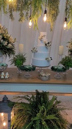 a table topped with a white cake surrounded by greenery and lite candles on top of it