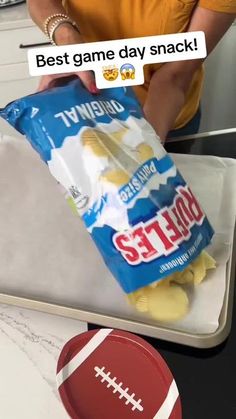 a person holding a bag of potato chips in front of a football on a counter