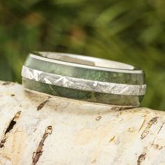 a wedding band with green and silver inlays sits on top of a tree trunk