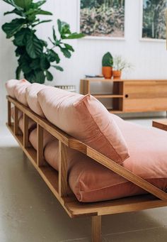 a wooden bench with pillows on it in front of a potted plant and other furniture