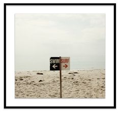 a red and white sign on the beach pointing in opposite directions to swim or surf