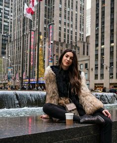 a woman sitting on top of a fountain next to tall buildings