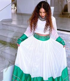 a woman in a white and green dress is standing on the steps with her hands behind her back