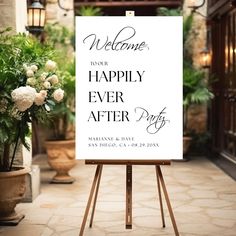 a welcome sign sitting on top of an easel in front of a building with potted plants