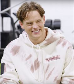 a man in a white hoodie smiles at the camera