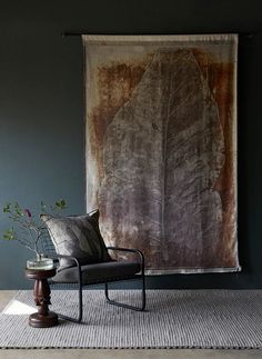 a chair sitting in front of a wall hanging with a large leaf design on it