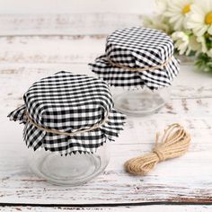 two small glass jars with black and white gingham fabric on them, sitting next to some daisies