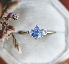 a blue ring with three stones on it sitting on top of a piece of cloth