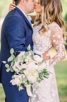 a bride and groom kissing in front of the trees at their outdoor wedding ceremony,