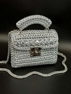 a white purse sitting on top of a black table next to a silver chain strap