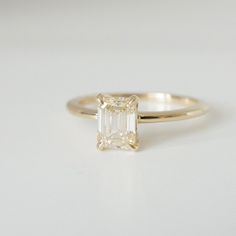 a yellow gold ring with an emerald cut diamond in the center, on a white surface