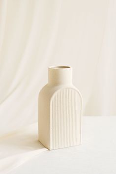 a white vase sitting on top of a table next to a white sheeted wall