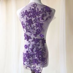 a mannequin with purple flowers on it's back and sides, in front of a white curtain