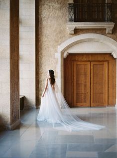 a woman in a wedding dress is standing by a door and looking at the floor