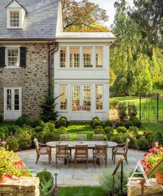 an outdoor dining area in front of a large house with stone walls and white trim