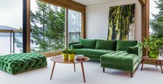 a living room filled with green furniture next to tall windows and trees in the background