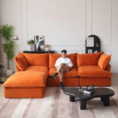 a man sitting on top of an orange couch in a living room next to a coffee table