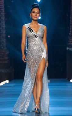 a woman in a silver dress with a white sash on the catwalk at a fashion show