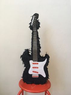 a guitar cake sitting on top of a red stool in front of a white wall