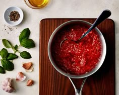 a pot filled with red sauce next to garlic and other ingredients on a cutting board