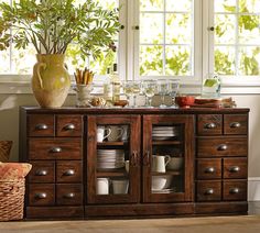 a wooden cabinet filled with lots of dishes and cups on top of it next to a window