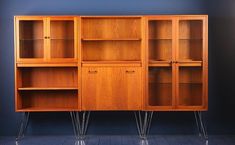 an old wooden cabinet with hairpin legs and glass doors on the front, against a blue wall