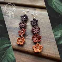 two crocheted flower earrings on top of a wooden table next to green leaves