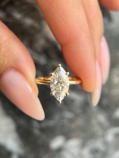 a woman's hand holding an engagement ring with a diamond in the middle, on top of her finger