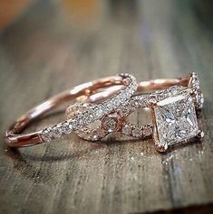 two wedding rings with princess cut diamonds on them sitting on top of a wooden table