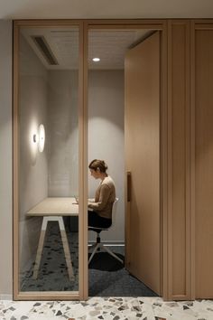 a woman is sitting at a desk in an office with glass walls and wooden doors