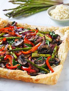 a vegetable tart on a cutting board next to asparagus and other vegetables