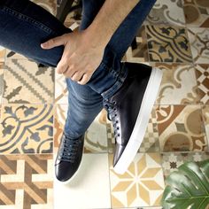 a man sitting on top of a wooden chair next to a green plant in front of a tiled floor