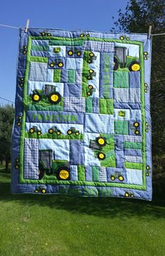 a quilt hanging on a clothes line in the grass with tractors and farm equipment painted on it