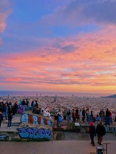 people are standing on top of a hill overlooking the city and ocean at sunset or dawn