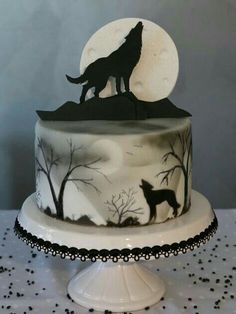 a white cake with black frosting and a wolf silhouette on top, sitting on a table