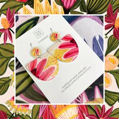 a pair of colorful earrings on top of a floral print paper with a white square frame