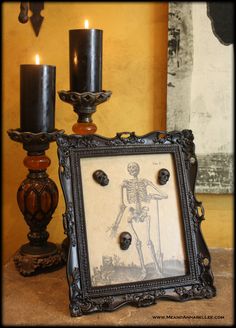 two candles are lit next to an old photo frame with a skeleton in the middle