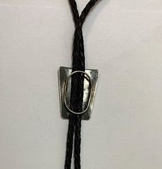 Beautiful Navajo handmade sterling silver Lowell Draper attributed bolo tie has braided black leather straps with handmade sterling silver tips. The center piece has a diagonally slanting linear design. Condition: Excellent! No damage or wear Artist: Unsigned Weight: 27 grams Measurements: 19 inches long (38 inches without the clip) Center piece is 1 3/4 inches tall x 1 1/2 inches wide Tips are 2 1/2 inches long Artisan Silver Lariat Bolo Tie, Adjustable Sterling Silver Lariat Bolo Tie, Silver Lariat Bolo Ties With Adjustable Length, Silver Lariat Bolo Tie With Adjustable Length, Handmade Southwestern Silver Bolo Ties, Artisan Lariat Bolo Tie With Adjustable Length, Adjustable Southwestern Bolo Tie For Formal Occasions, Western Silver Bolo Tie With Sliding Knot, Southwestern Style Adjustable Bolo Tie For Formal Occasions