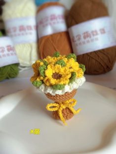 a small crocheted sunflower sitting on top of a white plate next to balls of yarn